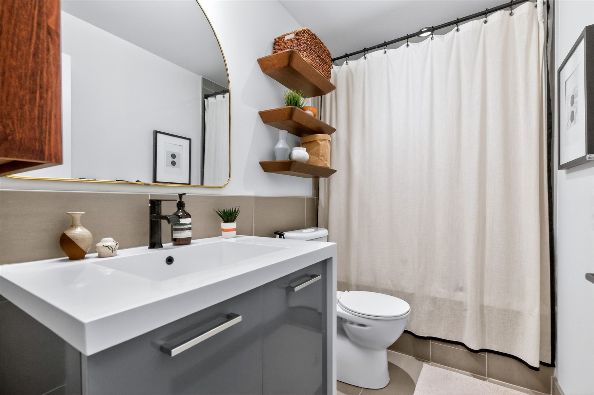 Bathroom with floating grey vanity, brass mirror and walnut shelves